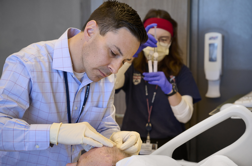 Dr. Steven Bagley administers a CAR T treatment while Lee Dengel prepares tubes for research samples.